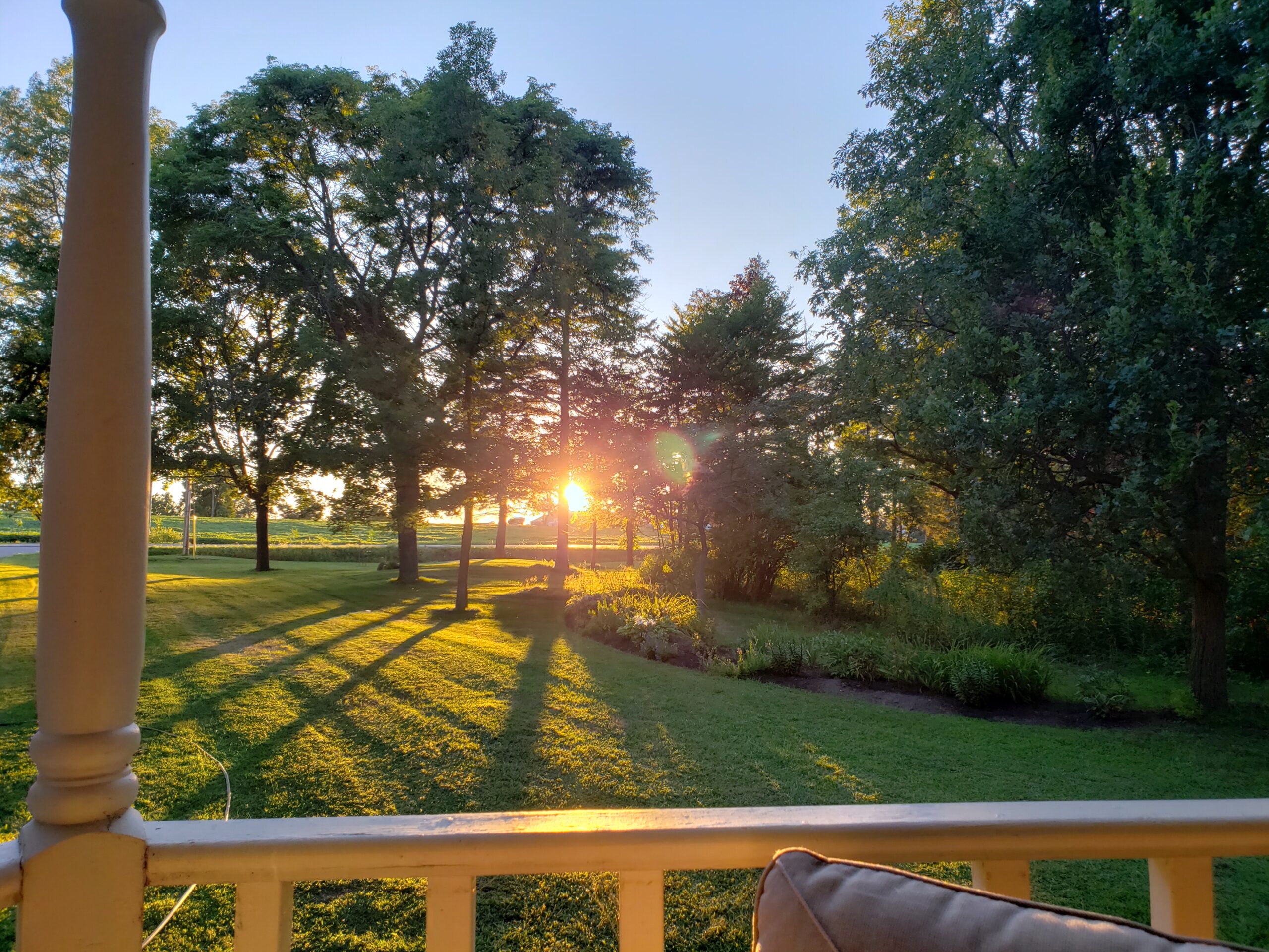 Sunset From the Front Porch – Ontario - Western Pride Woodworks Sunset viewed from the front porch of Derek Lunau's Ontario property, with golden light casting long shadows through mature trees.